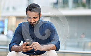 Indian business man using cell phone sitting on urban city street.