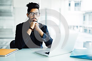 Indian business Man using laptop with hands hand on chin in his modern office