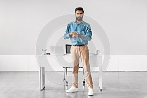 Indian businessman checking time, standing by office desk