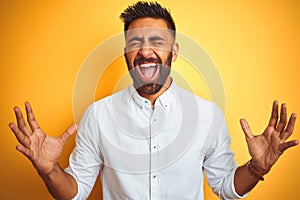 Indian businessman wearing white elegant shirt standing over isolated yellow background celebrating mad and crazy for success with