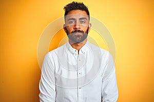 Indian businessman wearing white elegant shirt standing over isolated yellow background with serious expression on face