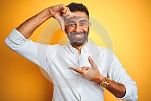 Indian businessman wearing white elegant shirt standing over isolated yellow background smiling making frame with hands and