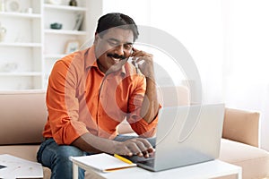 Indian businessman working from home, using laptop, have phone conversation