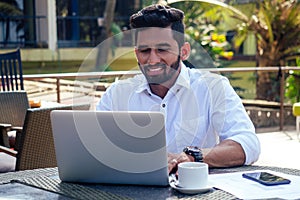 Indian businessman working on tablet computer copyspace on tropical beach cafe.freelancer man in a white shirt collar