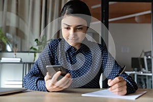 Indian businesswoman distracted for writing report check sms use smartphone