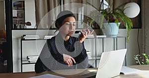 Indian businesswoman making call talking on speakerphone looking at computer