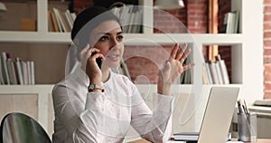 Indian businesswoman sit at desk talking to client on phone