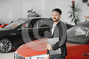 indian cheerful car salesman showing new car at showroom