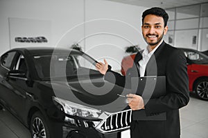 indian cheerful car salesman showing new car at showroom