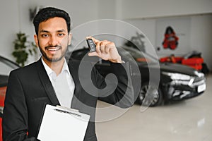 indian cheerful car salesman showing new car at showroom