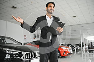 indian cheerful car salesman showing new car at showroom