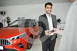 indian cheerful car salesman showing new car at showroom