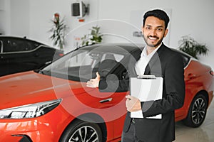 indian cheerful car salesman showing new car at showroom