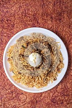 Indian Chicken Biryani dish is delicious and fragrant served on a white plate with egg in the middle, top view