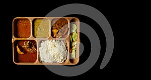 Indian chicken thali with rice dal chicken salad vegetable curry on a plastic segmented plate in black background