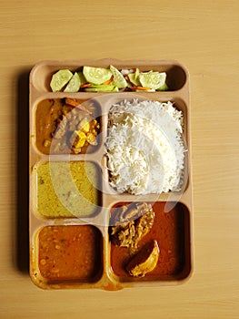 Indian chicken thali with rice dal chicken salad vegetable curry on a plastic segmented plate in wooden background