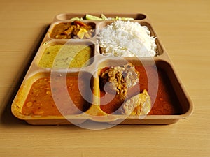 Indian chicken thali with rice dal chicken salad vegetable curry on a plastic segmented plate in wooden background