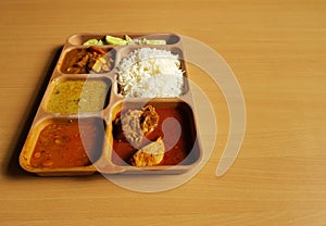 Indian chicken thali with rice dal chicken salad vegetable curry on a plastic segmented plate in wooden background