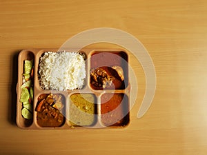 Indian chicken thali with rice dal chicken salad vegetable curry on a plastic segmented plate in wooden background