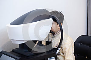 Indian child boy examining eyesight modern ophthalmology equipment in clinic. Patient kid male scan checkup iris examines