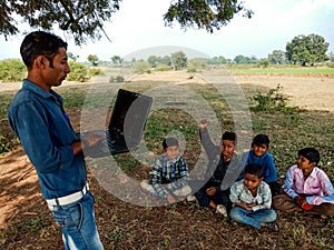 indian city boy giving laptop training to the village childrens at natural background in india January 2020