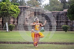 Indian classical Odissi dancer looks at the mirror during the Odissi dance recital against the backdrop of temple sculpture.