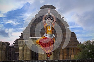 Indian Classical Odissi dancer pose in front of sun temple with sculptures in Konark, odisha, India.