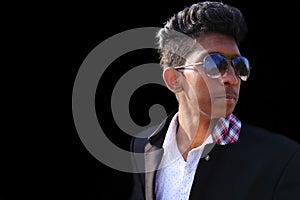 Indian cool young hipster man in a fashionable jacket in stylish sunglasses with trendy hairstyle on black background