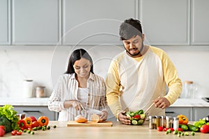 Indian Couple Cooking Food And Smiling Preparing Salad For Dinner