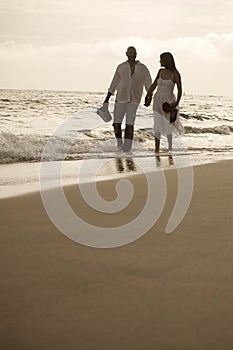 Indian couple holding hands walking on a beach together.