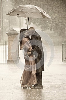 Indian couple kissing under an umbrella in the rain ki