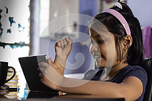 an Indian cute girl child playing video games at home with tablet