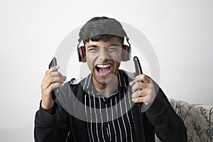 Indian cute teenager wearing black jacket, wireless headphone,holding cell phone,remote and keeping mouth open