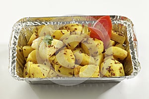 Indian dish fried potato with cumin in metal foil tray.