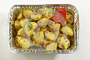 Indian dish fried potato with cumin in metal foil tray.