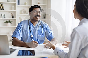 Indian doctor man listening female patient during meeting in office