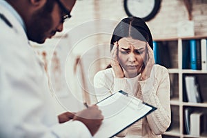 Indian doctor seeing patients in office. Doctor is listening to woman`s symptoms. Woman`s head hurts.