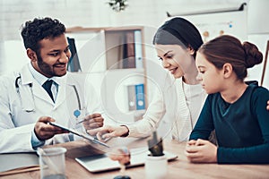 Indian doctor seeing patients in office. Doctor is showing clipboard to mother and daughter.