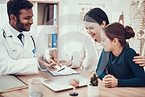 Indian doctor seeing patients in office. Doctor is showing tablet to mother and daughter.