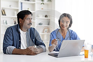 Indian doctor woman showing laptop screen to patient during appointment in clinic