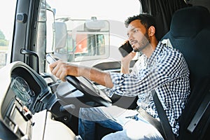 Indian Driver talking by mobile phone while sitting in cabin of big modern truck.