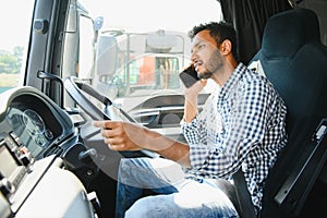 Indian Driver talking by mobile phone while sitting in cabin of big modern truck.