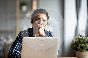 Indian employee sitting at desk yawning feels unmotivated and tired