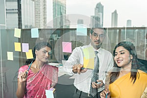 Indian employees sticking reminders on glass wall in the office photo