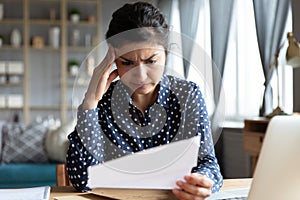 Indian ethnicity woman sit at desk reading letter feels disappointed