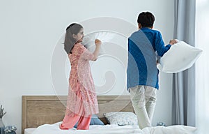 Indian family, brother and sister with traditional clothes having fun playing pillow fight, two children standing on bed together