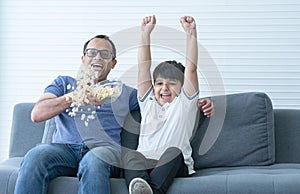 Indian family, excited father and child son watching tv or football match, shouting, celebrating team win, sitting on sofa with