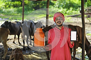 Indian farmer holding milk bottle in hand and showing mobile phone blank screen