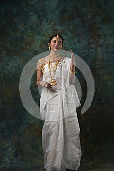 Indian female model wearing a shite traditional saree and gold jewellry sporting a bengali bnodini look