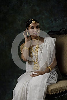 Indian female model wearing a shite traditional saree and gold jewellry sporting a bengali bnodini look